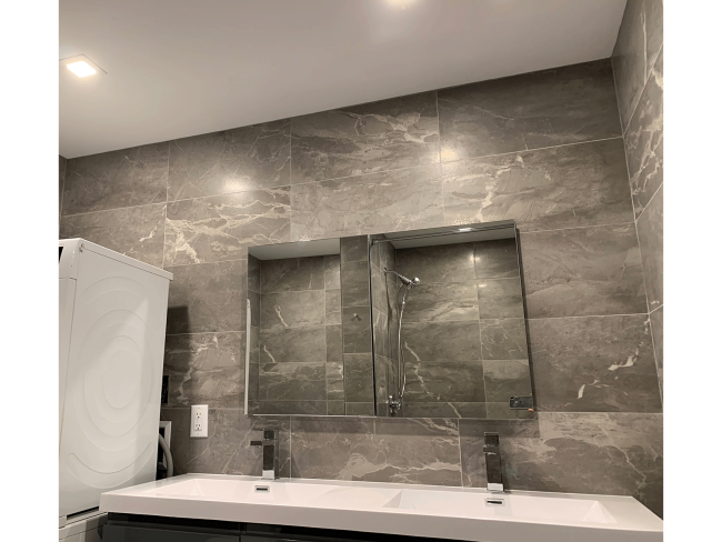 Bathroom vanity with mirrors, gray marble walls, and double sink.