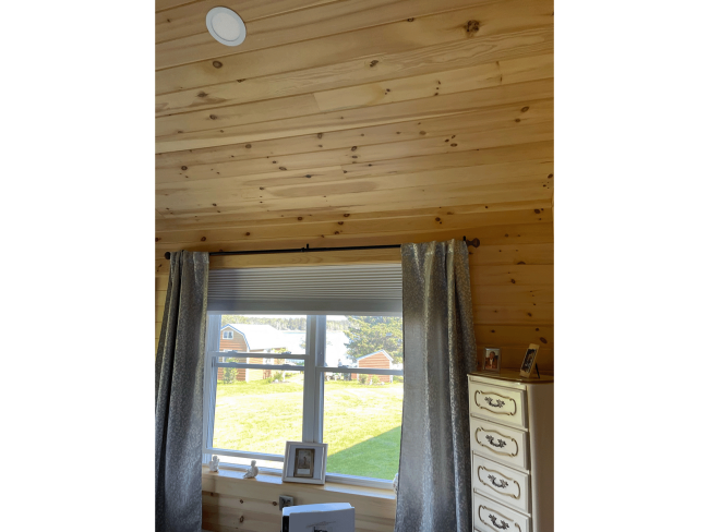 Wood ceiling and walls and a window that looks out upon a lawn.
