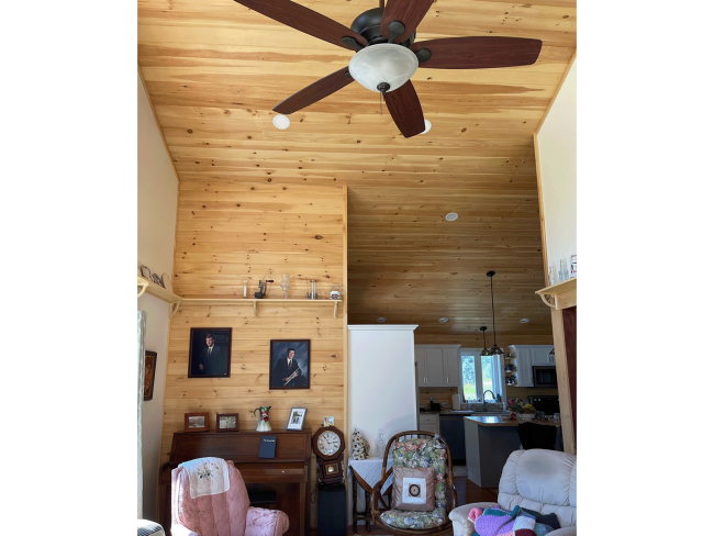 Wood walls and ceiling in the living room with fan.
